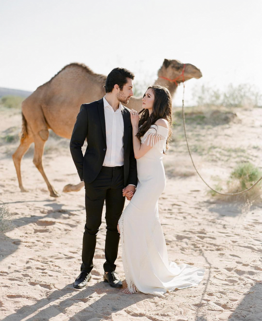 Man and woman staring at each other lovingly with a camel in the background